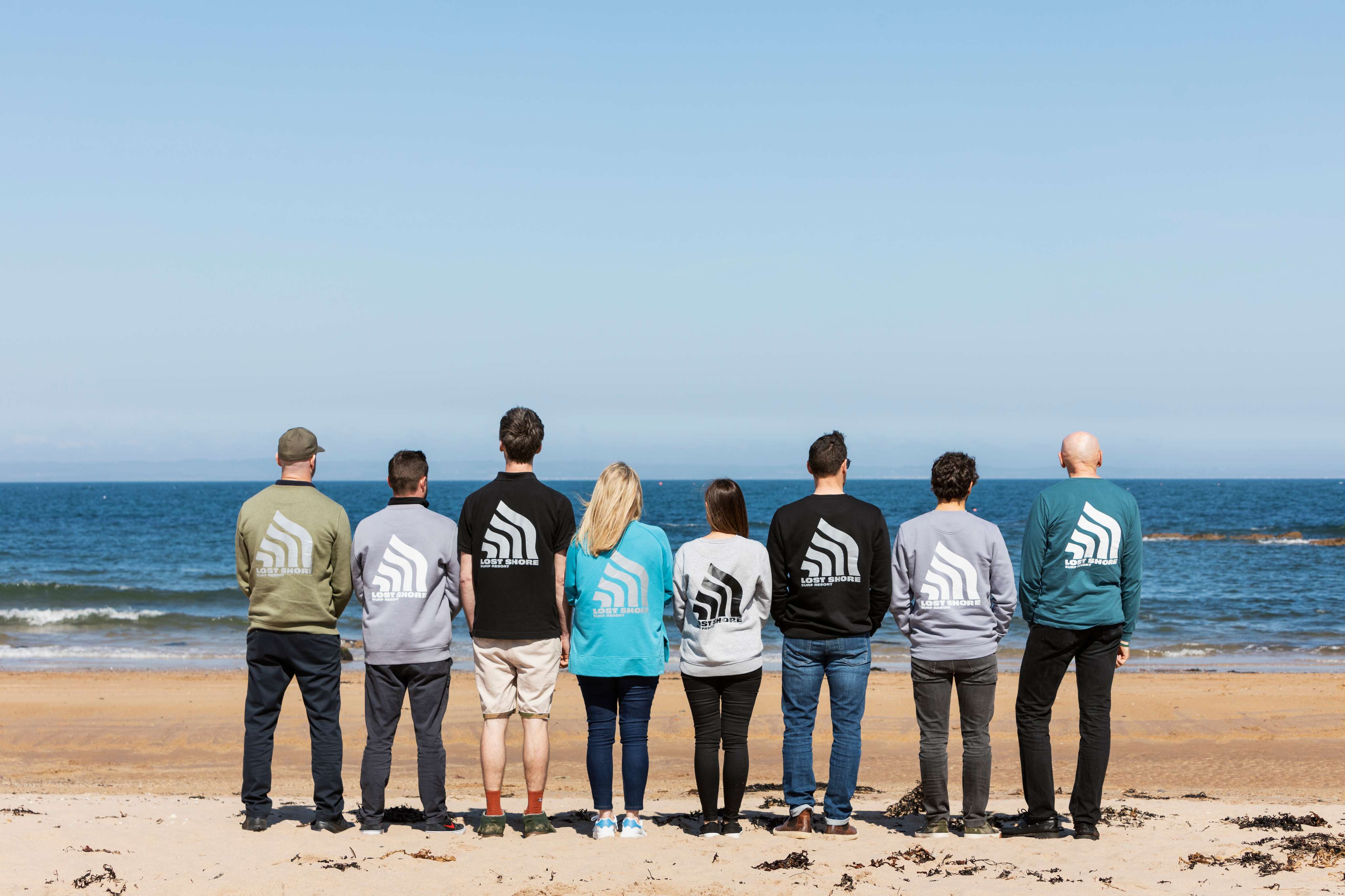 People standing on the beach with the backs to the camera, facing the ocean